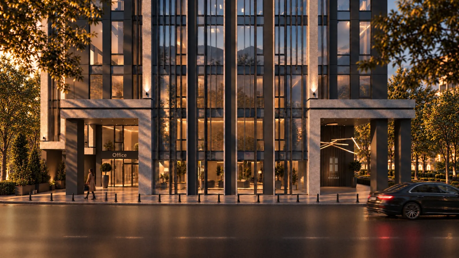 The double-height entrance colonnade at night, lit warm from within, a dark car at the kerb and wet paving reflecting the light.