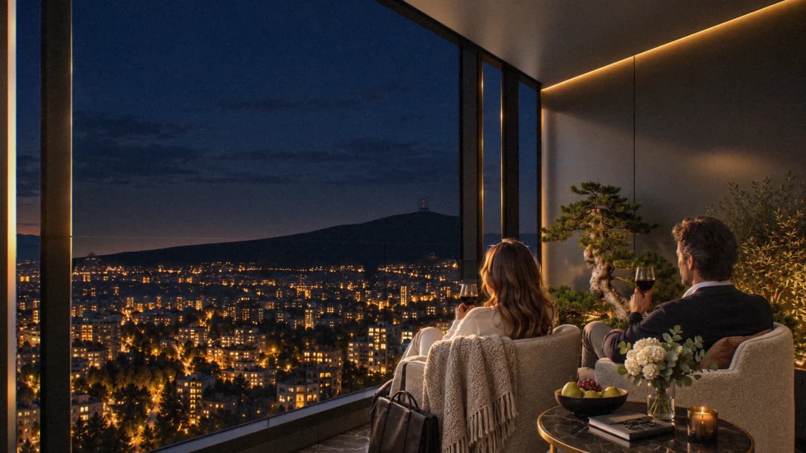 A couple on the terrace at night, the city spread out below in lights and the dark line of the mountain behind.