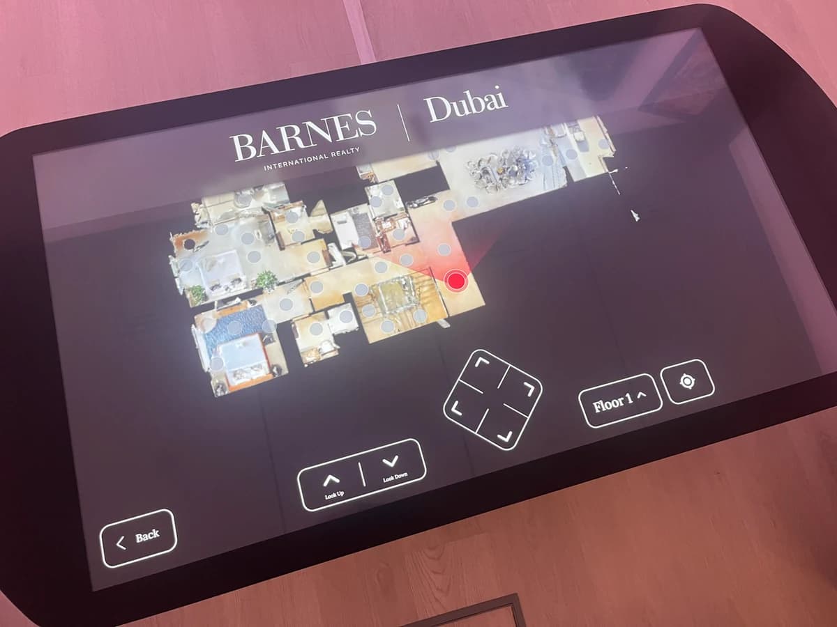 The touchscreen table in the BARNES Dubai room, running a floor-plan navigator: an overhead plan of an apartment under the BARNES Dubai lockup, dotted with viewpoint markers and one active red point, with Look Up, Look Down, a directional pad and a Floor 1 selector along the bottom.