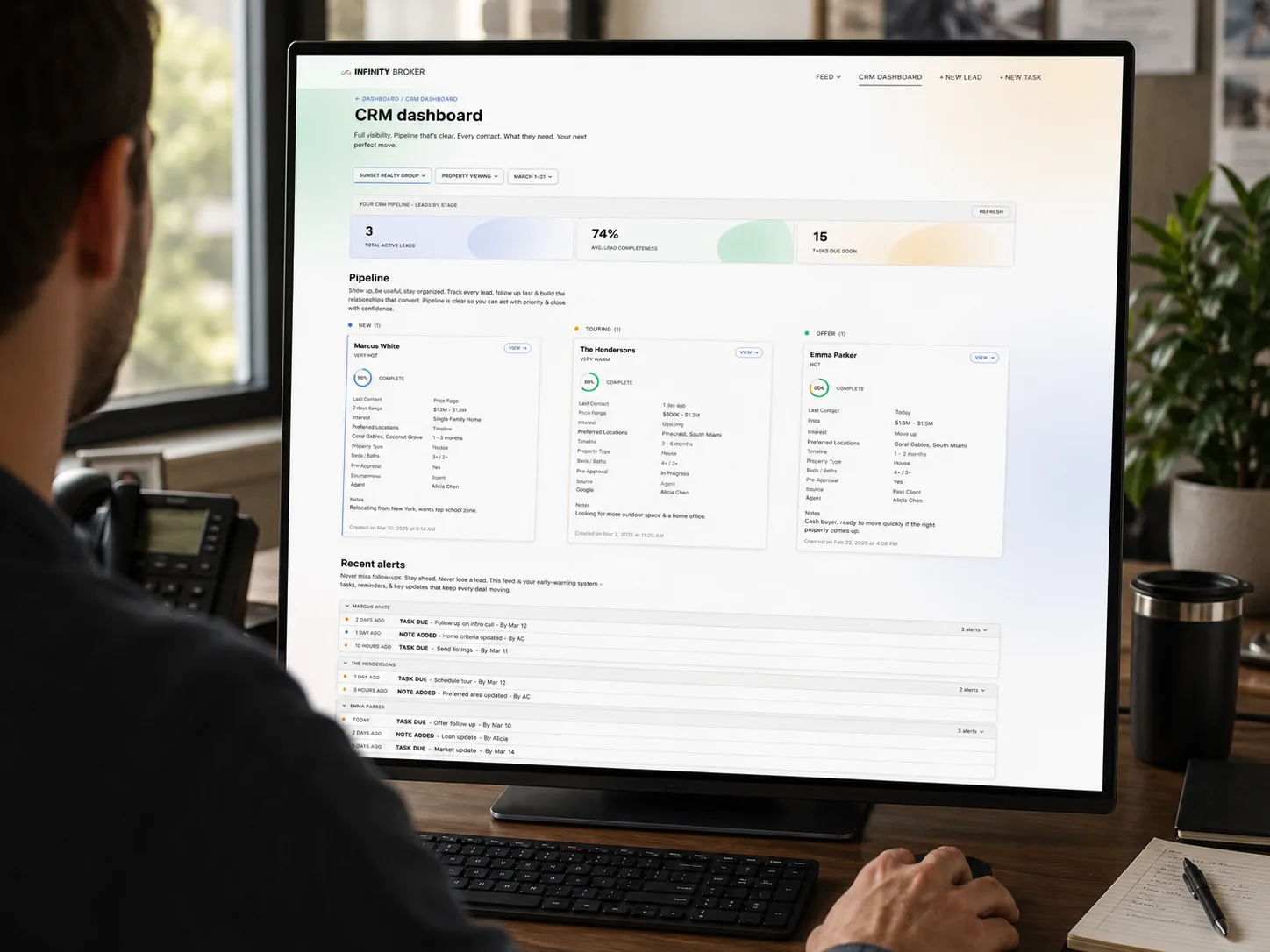 Over-the-shoulder view of a broker at a desktop monitor using the Infinity Broker CRM dashboard, a lead pipeline in New / Touring / Offer columns.