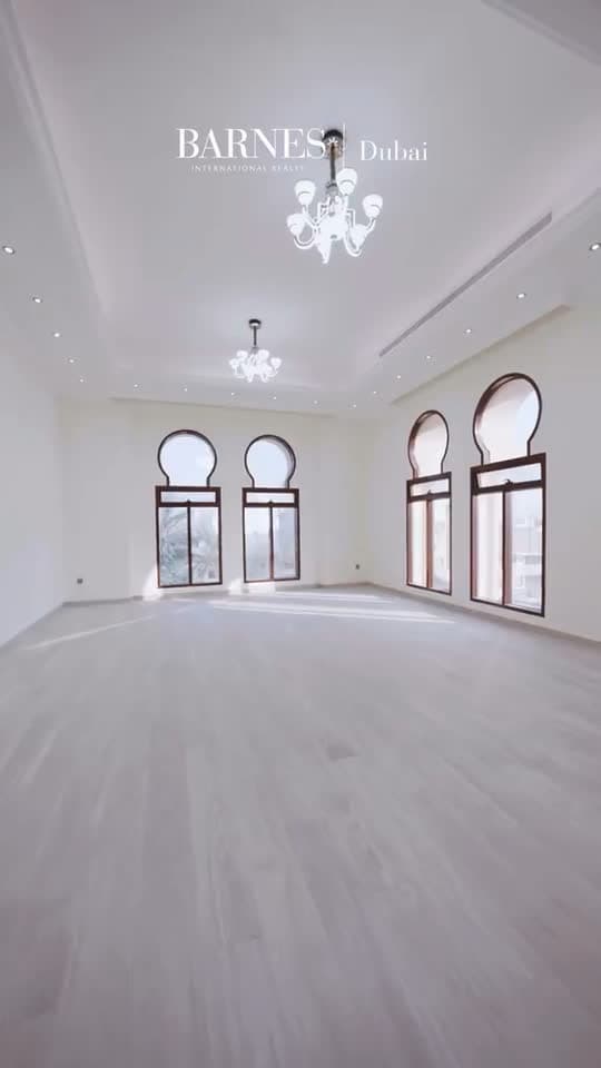 An empty villa bedroom with arched windows, bare carpet and a chandelier.