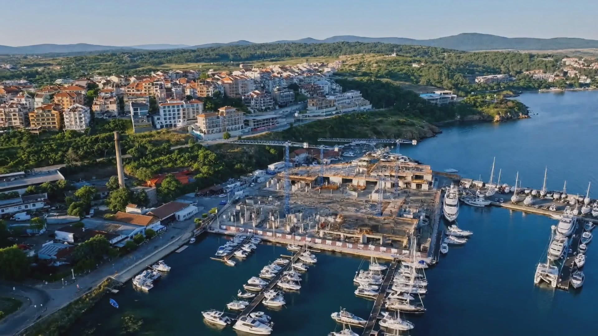 Aerial view of the Sozopol marina with the residences under construction, bare concrete frames and cranes beside the moored boats.