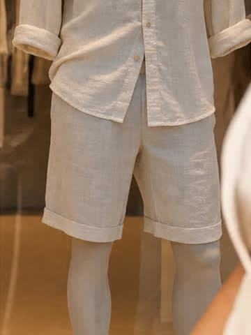 A shop mannequin in a linen shirt and rolled linen shorts, a clothes rail behind it.