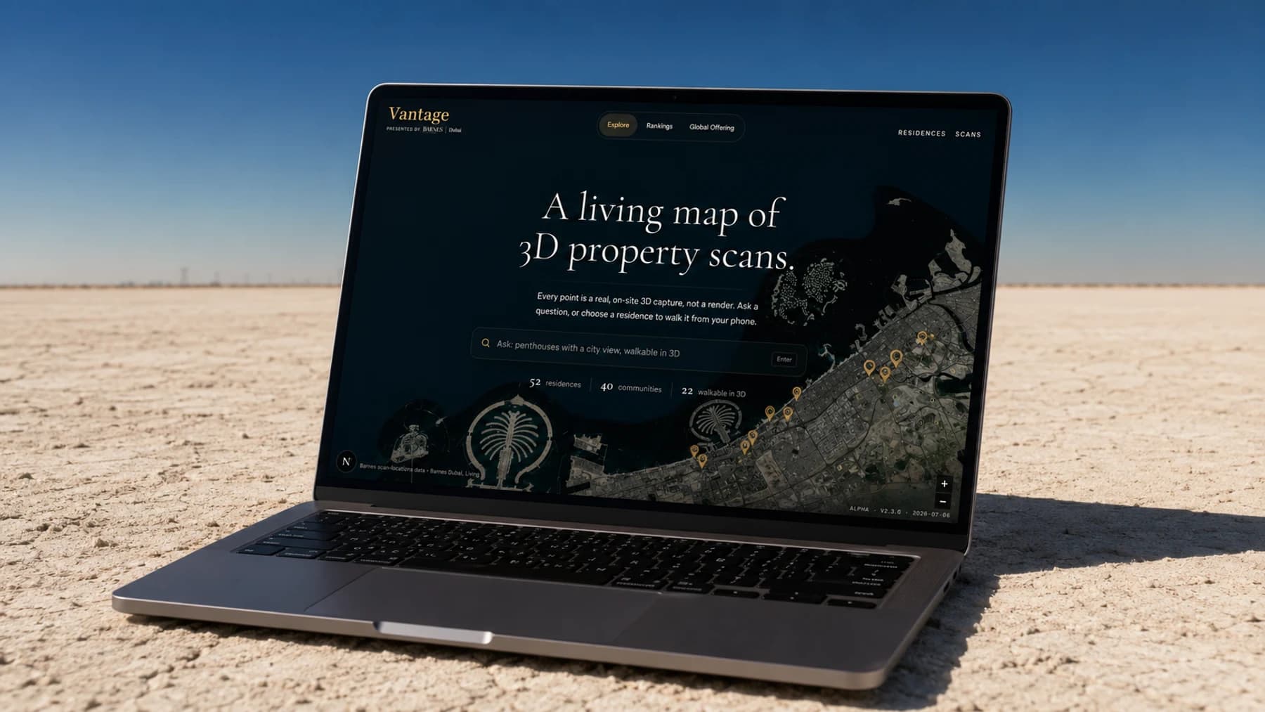 Barnes Vantage open on a laptop resting on a vast pale desert floor under a deep blue sky, the screen showing a dark satellite map of the Dubai coastline with the Palm and the World islands, the headline 'A living map of 3D property scans.', a natural-language search bar, and a stat row reading 52 residences, 40 communities, 22 walkable in 3D.